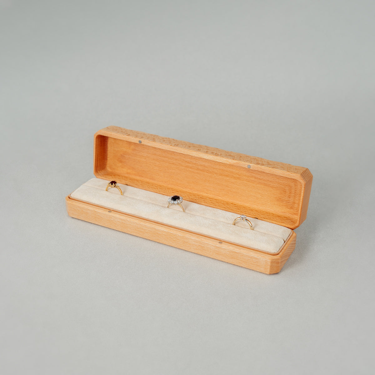 Open Jewellery Box made of beech wood while The interior of the box is lined with soft velvet with three rings placed inside.