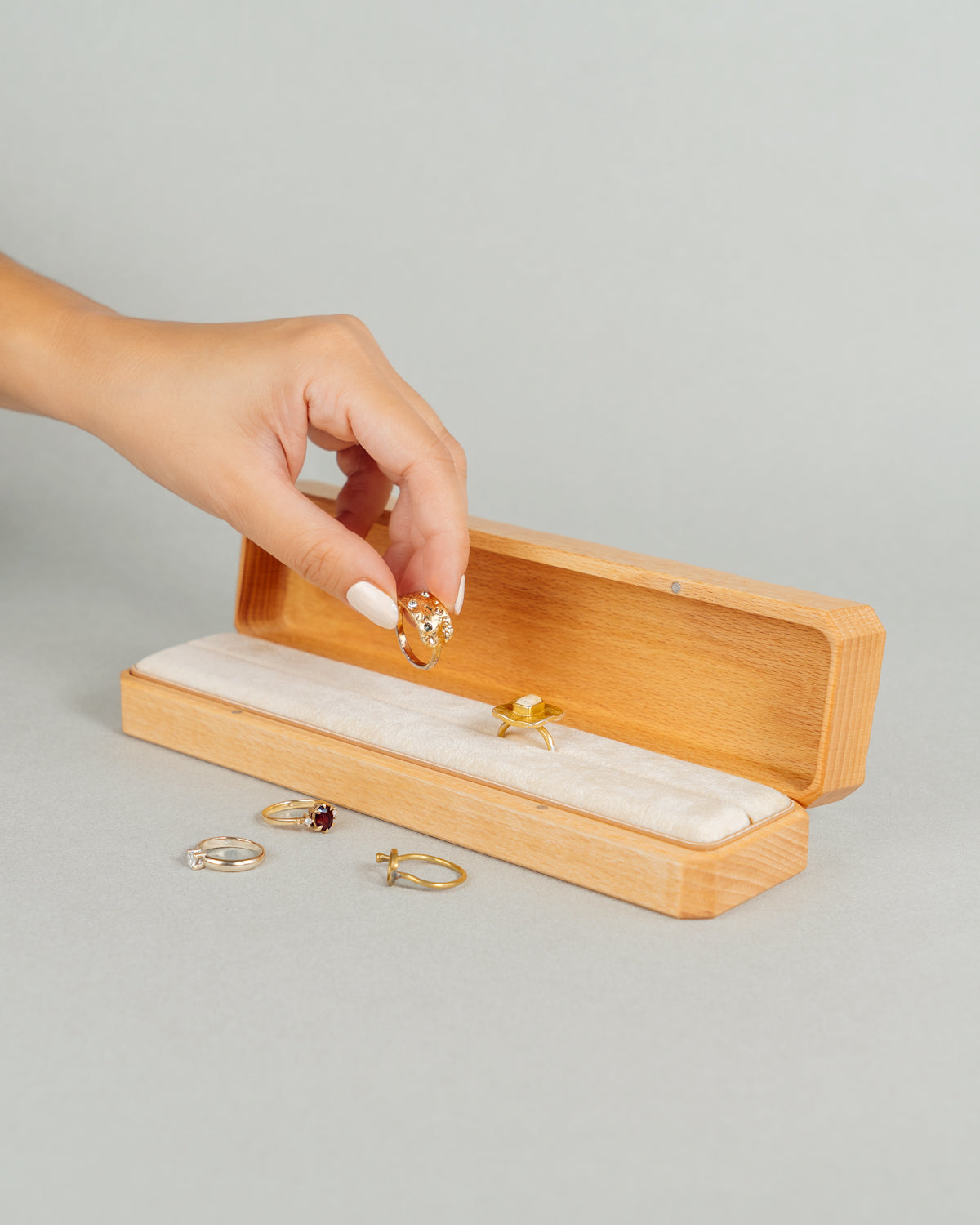 An hand is placing a ring in a long jewellery box made of beech wood and Open Jewellery Box made of walnut wood the interior of the box is lined with soft velvet.